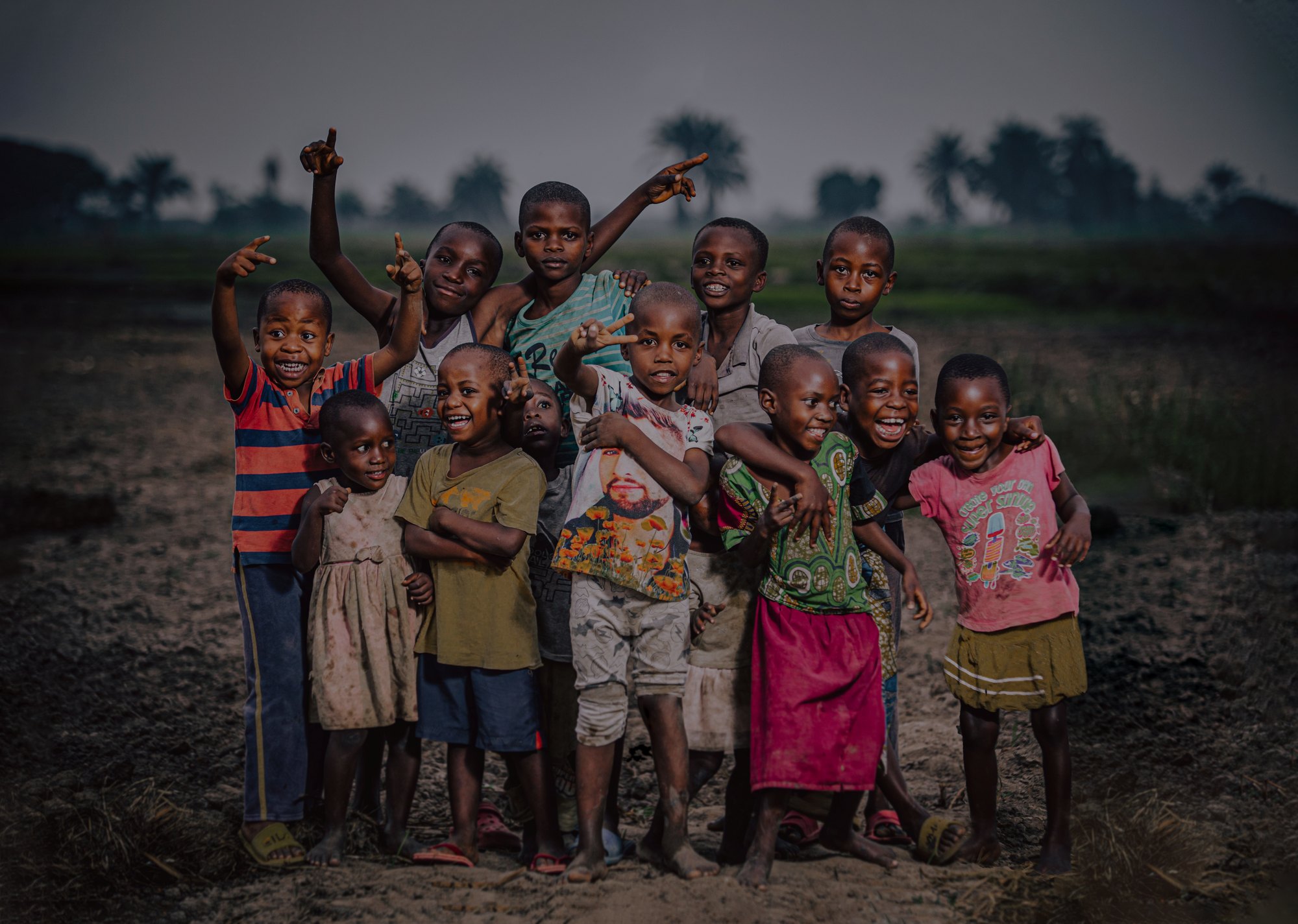A group of children waving and pointing at the camera at dusk in Zambia